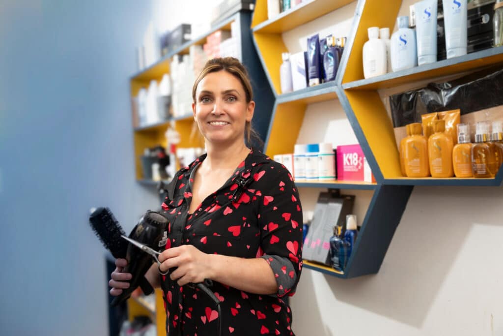Portrait of a lady holding a blow dryer, scissors and brush smiling
